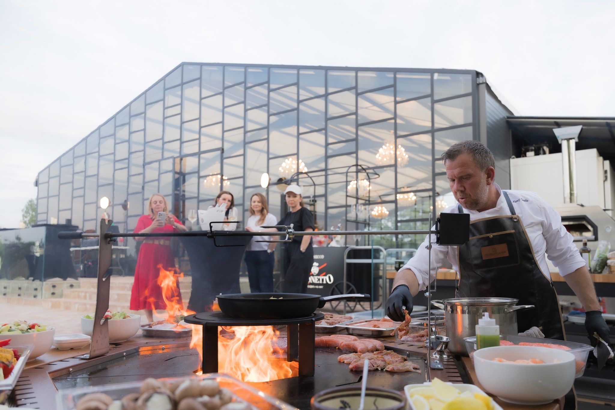 Invitați adunați în fața halei de sticlă, lângă o stație de live cooking, la un eveniment